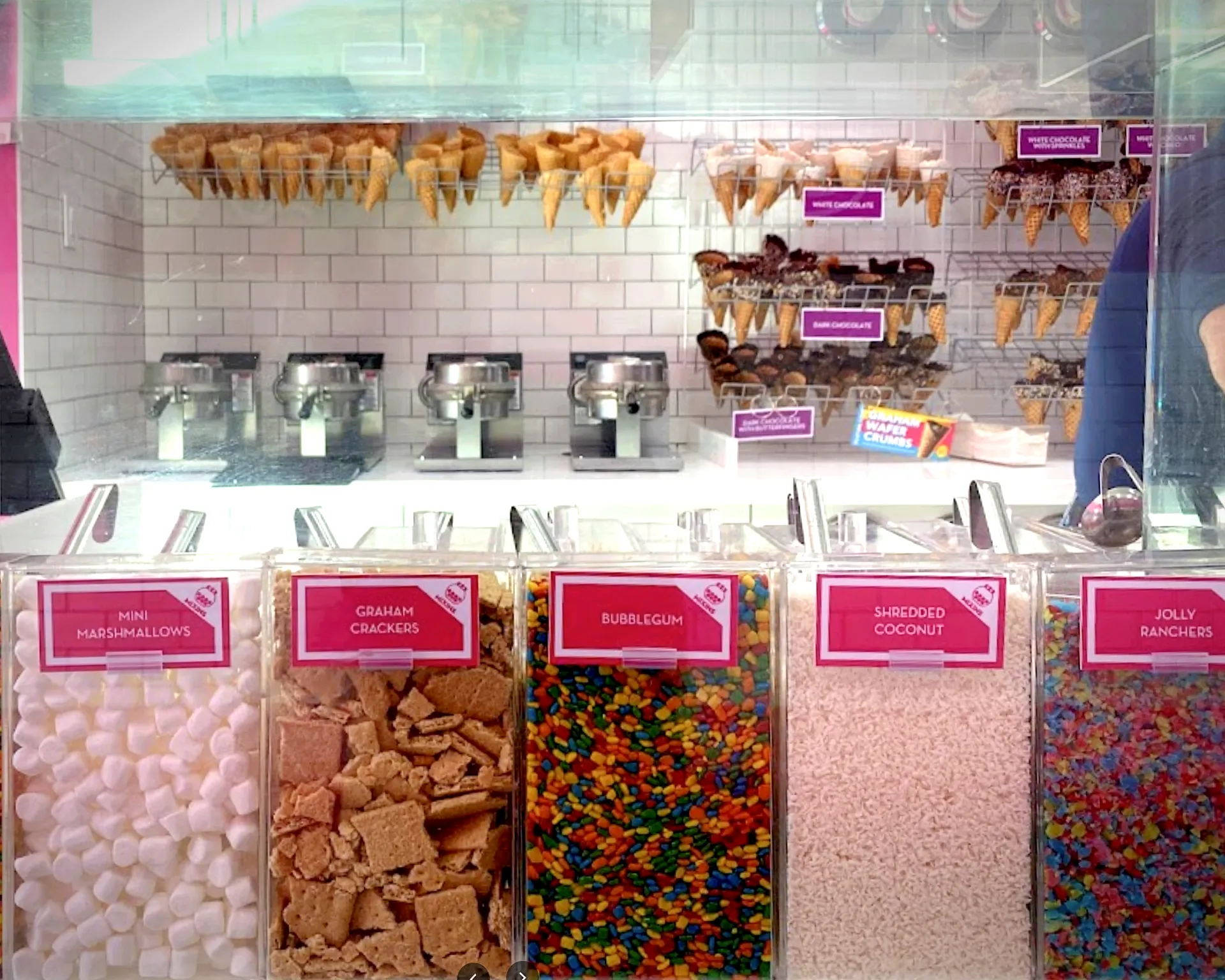 Various cups, cones, and candy on display in front of the custom cold shelf and white subway tile backsplash.